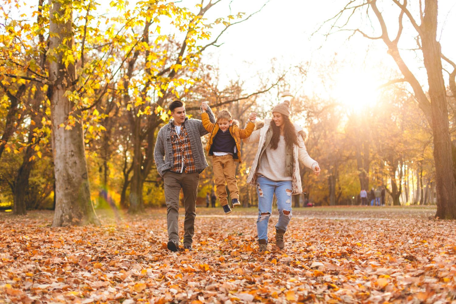Vater, Kind und Mutter bei einem Waldspaziergang im Herbstlaub