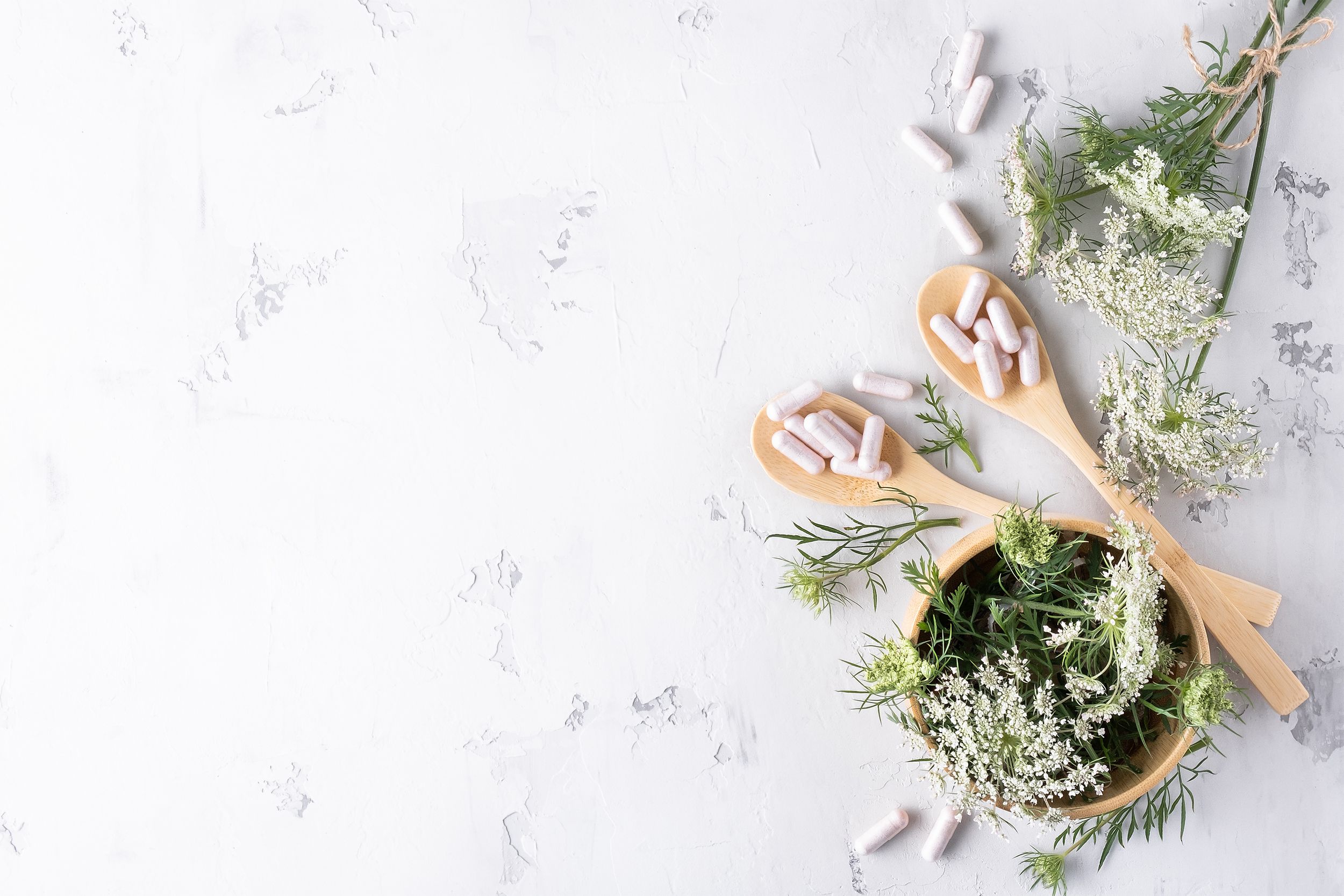 Tabletten liegen auf Holzlöffeln umgeben von Pflanzen